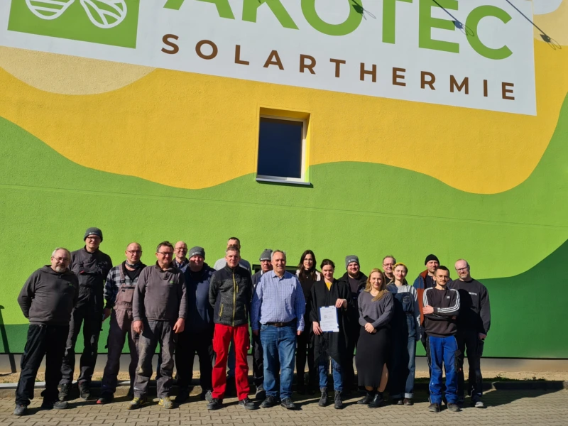 Gruppenfoto des AKOTEC Solarthermie-Teams vor einem farbenfrohen Firmengebäude mit großem Logo. Symbol für Teamarbeit, Innovation und den gemeinsamen Einsatz für nachhaltige Energielösungen.