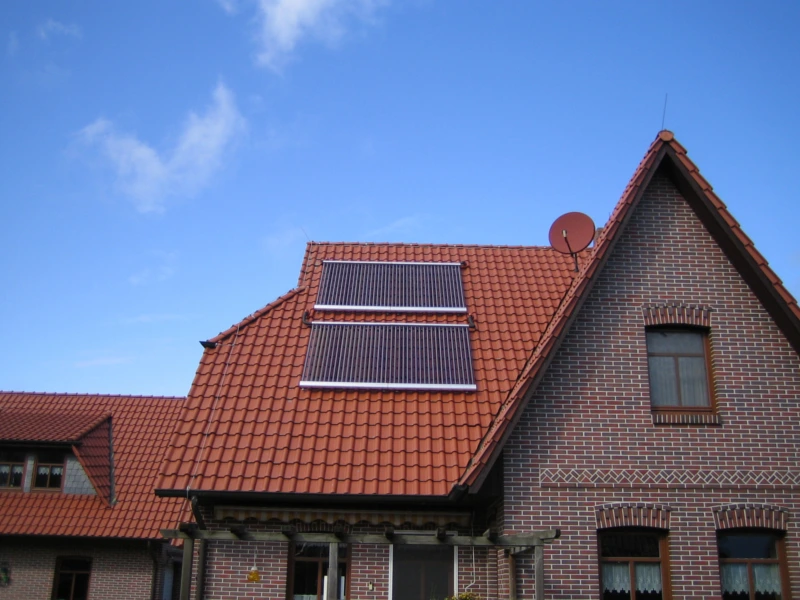 Backsteinhaus mit rotem Ziegeldach und zwei Solarthermie-Kollektoren für nachhaltige Warmwasserbereitung und Heizungsunterstützung. Symbol für mehr Unabhängigkeit und umweltfreundliche Energieversorgung.