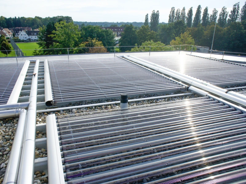 Großflächige Solarthermieanlage mit Vakuumröhrenkollektoren auf einem Flachdach, umgeben von einer grünen Landschaft. Symbol für nachhaltige Energiegewinnung und effiziente Nutzung von Sonnenenergie im Rahmen der neuen BEG-Förderung 2021