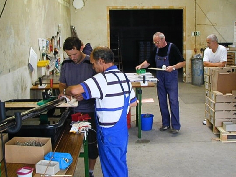 Mehrere Männer arbeiten in einer Werkstatt an Solarkomponenten mit Werkzeugen und Materialien auf Werkbänken.