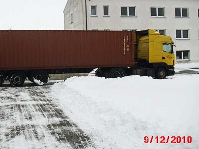 Gelber LKW mit braunem Container im Schnee vor einem Firmengebäude, Datum 9. Dezember 2010.