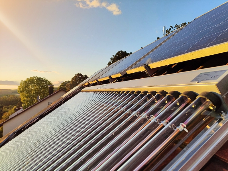 AKOTEC Solarthermieanlage mit Vakuumröhren und Photovoltaikmodulen auf einem Ziegeldach im Sonnenuntergang, ideal für nachhaltige Energiegewinnung und umweltfreundliche Wärmeversorgung.