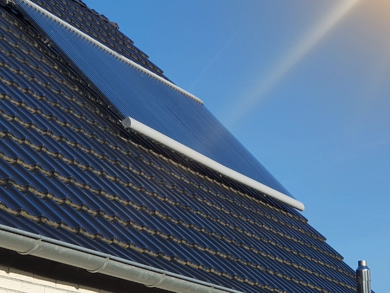 Das Bild zeigt eine Solarthermie-Anlage mit Vakuumröhrenkollektor, der auf einem dunkel gedeckten Schrägdach eines Wohnhauses installiert ist. Die Solarröhren sind in einem optimalen Winkel zur Sonne ausgerichtet, um maximale Effizienz bei der Nutzung von Solarenergie für Warmwasserbereitung und Heizungsunterstützung zu gewährleisten.