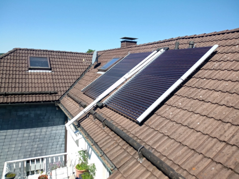 Solarthermieanlage mit Vakuumröhrenkollektoren auf einem Ziegeldach eines Einfamilienhauses installiert. Nachhaltige Lösung zur effizienten Warmwasserbereitung und Heizungsunterstützung durch Sonnenenergie.