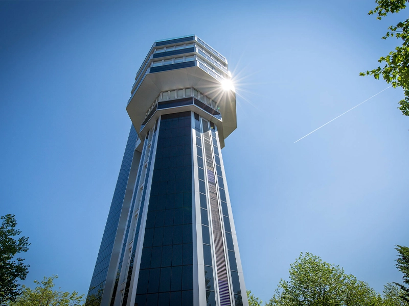 Moderner Aussichtsturm in Radolfzell mit glänzender Glasfassade und Solartechnik von AKOTEC Solarthermie, strahlende Sonne am blauen Himmel, nachhaltige Architektur und innovative Solarlösung im urbanen Umfeld.