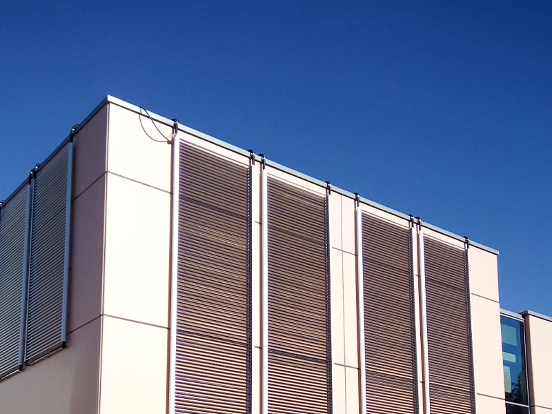 Moderne Gewerbegebäude-Fassade mit vertikal montierten Solarkollektoren vor klarem, blauem Himmel.