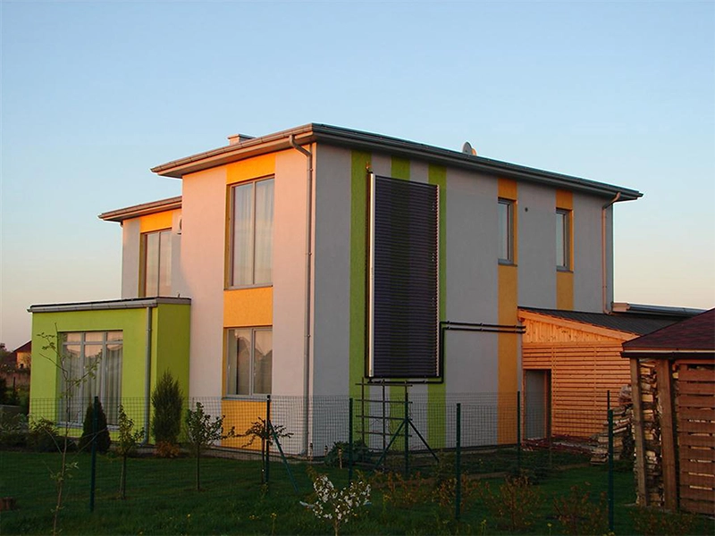 Modernes zweistöckiges Wohnhaus mit Solarthermie-Anlage an der Fassade, umgeben von Garten und Holzschuppen.