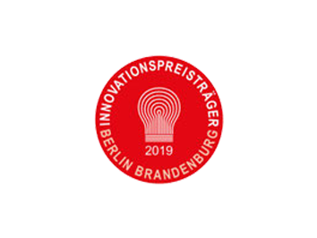 Das Bild zeigt das Logo des Innovationspreisträgers Berlin Brandenburg 2019 in Form eines roten Kreises. In der Mitte befindet sich ein stilisiertes Glühbirnen-Symbol, das für kreative Ideen und technologische Innovation steht, mit der Jahreszahl ‚2019‘ darunter. Der Schriftzug ‚INNOVATIONSPREISTRÄGER BERLIN BRANDENBURG‘ umrahmt das Logo.